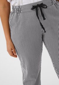 Pantalons rayés noir et blanc avec une taille élastique, fermeture à cordon de serrage et poches latérales ; le tissu semble doux avec une texture lisse.