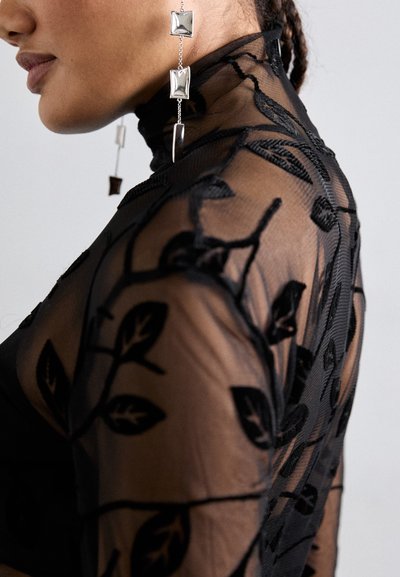 Black sheer top with floral embroidery, high neck, and fitted design. Silver drop earrings with rectangular and square accents.