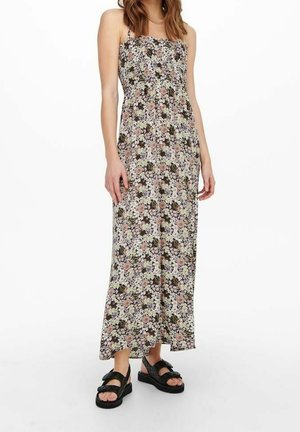 Femme portant une robe longue sans manches à imprimé floral avec fines bretelles et des sandales à plateforme noires ornées de nœuds.