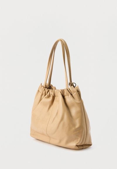 Μπεζ τσάντα tote από μαλακό δέρμα με στρογγυλεμένη κορυφή και δύο μακριές λαβές, εμφανίζεται σε απλό ανοιχτό φόντο.