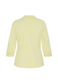 Blazer jaune pâle avec manches trois-quarts froncées, taille cintrée et simple couture au dos.