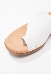 White leather slide sandal with an open toe. Features a beige suede footbed and stitched detailing along the edge. Rubber sole.