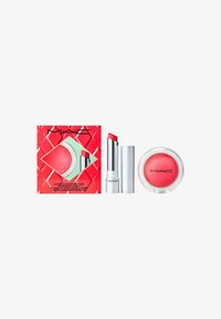 Il set di trucco MAC include un rossetto argentato lucido, un blush rosso cremoso in un contenitore trasparente e una scatola di imballaggio rossa con motivo geometrico.