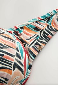 Daudzkrāsains krūšturis ar abstraktu rakstu kombināciju zaļa jūras krāsā, koraļļos un melnā krāsā, regulējamām lencēm un zelta krāsas detaļu.