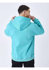 Sudadera con capucha turquesa con un bolsillo canguro, puños y dobladillo acanalados. Fabricada en un tejido suave con una textura lisa, se muestra desde la parte de atrás.