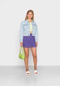 Casaco de ganga, azul claro; top curto verde limão; saia mini roxa com padrão ondulado; sandálias brancas; mala verde.