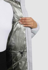 Leichte weiße Jacke mit einem glänzenden silbernen Futter, die eine strukturierte Oberfläche und ein Kordelzug-Detail aufweist.