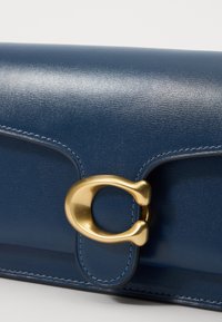 Clutch in pelle blu scuro con una superficie liscia, caratterizzato da una chiusura in metallo dorato prominente e dettagli cuciti.