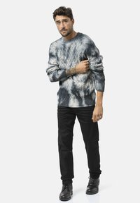 Strickpullover mit Struktur in Blau- und Grautönen mit einem Rautenmuster, kombiniert mit schwarzen Hosen und schwarzen Schnürstiefeln.