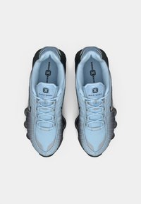 Svjetloplave atletske cipele s crnim akcentima i sivim detaljima, s teksturiranom gornjom površinom, vezicama i vidljivim elementima amortizacije.