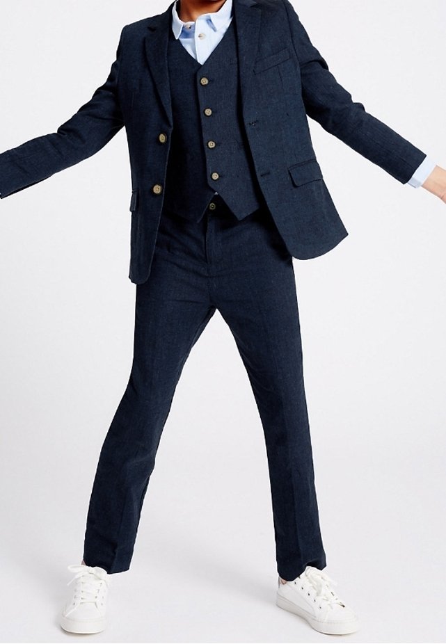 Granatowy, dopasowany garnitur trzyczęściowy wykonany z fakturowanej tkaniny, składający się z marynarki z czterema guzikami, kamizelki i slim fit spodni. Białe sneakersy.