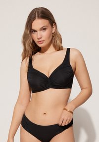 Conjunto de bikini negro con diseño fruncido, tirantes anchos y ajustables, y una textura suave. Detalles notables incluyen un frente recogido en la parte superior.