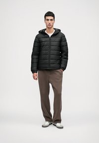 Mustmust mustriga jope horisontaalsete õmblustega, kapuutsiga ja esise tõmbega, kantud beežide laiatõsiste pükste ja mustade aktsentidega valgete tossudega.