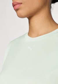 Jasno miętowa koszula z krótkim rękawem, okrągłym dekoltem i małym białym logo Puma na lewej piersi. Miękka tekstura materiału.