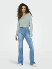 Jeans de campana de color azul claro combinados con una blusa de manga larga de ajuste relajado en gris claro. El conjunto presenta texturas sutiles y un diseño casual.