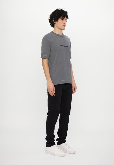 T-shirt de manga curta cinza e branca com riscas, gola redonda e logótipo preto, combinada com calças pretas e sapatilhas brancas.