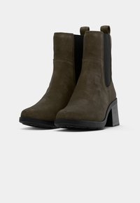 Bottines en daim marron avec un talon noir épais et des panneaux élastiques sur les côtés. Présente une texture lisse avec un design minimaliste.