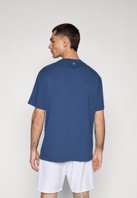 Mørkeblå t-shirt med rund halsudskæring, korte ærmer og en lille knapdetalje bagpå. Designet med en afslappet pasform.