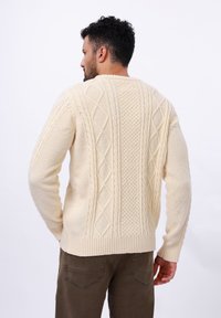 Pull en tricot couleur crème avec des motifs en relief et en losange, tissu texturé, et poignets côtelés, doté d'un col rond.