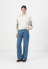 Felpa crema con grafiche nere sulle maniche, abbinata a jeans a gamba larga azzurri e sneakers con plateau nere.