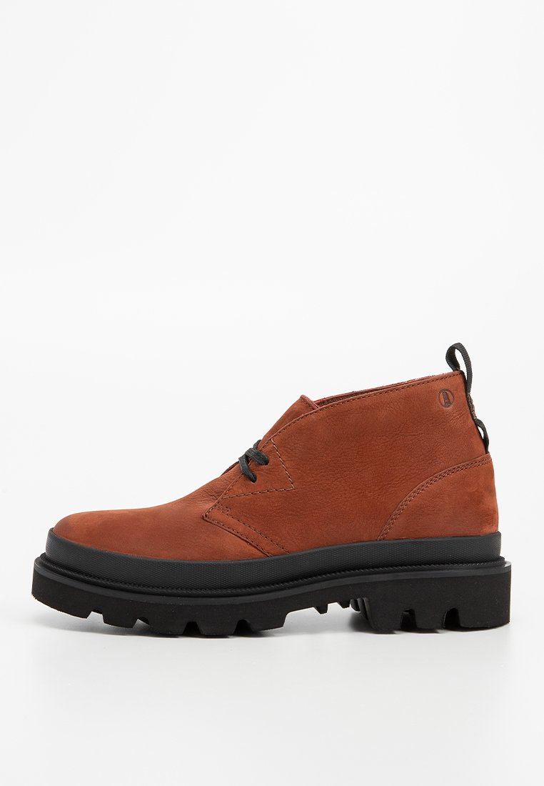 Botte cheville en cuir marron avec semelle épaisse noire et lacets noirs, dotée d'une languette au niveau du talon.