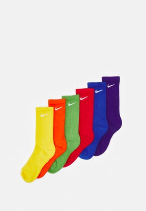 Sete pares de meias até ao joelho em cores vibrantes: amarelo, laranja, verde, vermelho, azul e roxo, com o logótipo branco da Nike em cada uma.