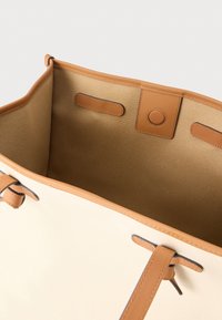 Borsa tote in tela color crema con dettagli in pelle marrone chiaro. Interno con tessuto liscio, chiusura a calamita e ulteriori manici in pelle marrone chiaro.
