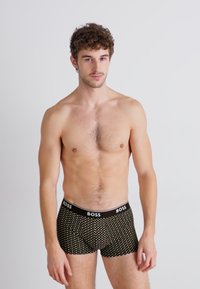 Schwarze Boxershorts mit einem gemusterten Design, ausgestattet mit einem Logo-Elastikbund und einem figurbetonten Schnitt. Das Material wirkt glatt, dehnbar und leicht.