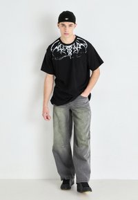 Black cotton t-shirt featuring a white graphic design on the chest, paired with faded gray wide-leg jeans and black sneakers.