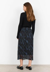Zwarte geribbelde langemouwen top gecombineerd met een vloeiende midi-jurk in zwart en blauw met een patroon. De jurk heeft een geplooide structuur en een semi-doorzichtige zoom.