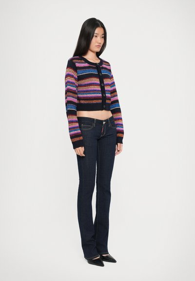 Cárdigan corto a rayas en azul marino oscuro con rayas horizontales multicolores. Combinado con jeans de campana en azul oscuro y zapatos negros de punta.