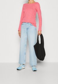 Helles rosa Langarmoberteil, lockerer Schnitt; hellblaue weit geschnittene Jeans; schwarze Stofftasche; blau-weiße Sportschuhe.