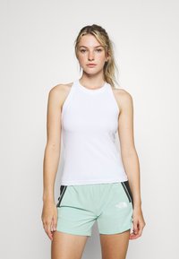 Top de tanque branco com um design de gola alta, combinado com calções verdes-menta com riscas laterais pretas e um logótipo.