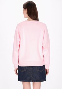 Rózsaszín pulóver laza szabással, bordázott mandzsettákkal és szegéllyel, valamint raglán ujjakkal, amelyet sötét farmer szoknyával párosítanak, mely hátsó zsebekkel rendelkezik.