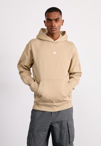 Felpa beige con cappuccio, tasca frontale e piccolo logo. Realizzata in tessuto morbido, presenta una vestibilità comoda e orlo a costine. Abbinata a pantaloni cargo grigi.