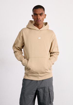 Felpa beige con cappuccio, tasca frontale e piccolo logo. Realizzata in tessuto morbido, presenta una vestibilità comoda e orlo a costine. Abbinata a pantaloni cargo grigi.