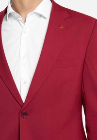 Blazer rosso con una texture liscia, chiusura a un bottone, rever a punta e taschino sul petto; presenta un piccolo dettaglio ricamato giallo.