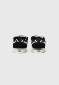 Schwarze und graue Sneakers im Tarnmuster mit einer strukturierten Wildlederferse, weißer Gummisohle und Logo auf der Rückseite.