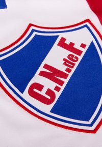 Geborduurd schildlogo in blauw en wit met rode accenten, met "C.N. de F." prominent weergegeven op een witte achtergrond.