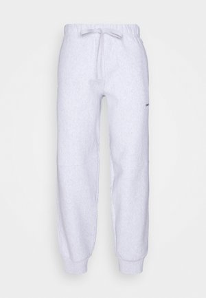 Pantalons de survêtement gris clair en tissu doux et texturé, avec une taille élastique, un cordon de serrage et des poignets côtelés aux chevilles. Petit logo sur le côté.