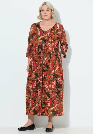 Robe longue paisley rouge avec des manches 3/4, un col en V et une taille froncée. Présente des motifs noirs, orange et blancs. Associée à des chaussures plates noires.