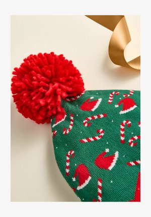 Green knitted beanie with red pom-pom, featuring white candy canes and red Santa hats in a repeating pattern. Smooth texture, festive design.