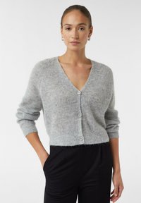 Lichtgrijze cardigan met een V-hals, knoopsluiting aan de voorkant en geribbelde manchetten. Zachte textuur, cropped ontwerp en lichte nadruk op fuzzy details.