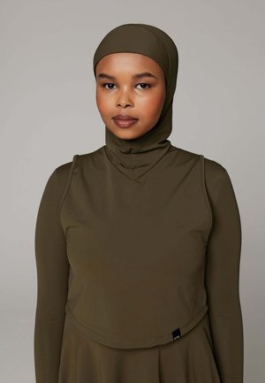 Vrouw draagt een bescheiden olijfgroene badkleding set met een aansluitende capuchon en lange mouwen, kijkt naar voren tegen een neutrale achtergrond.