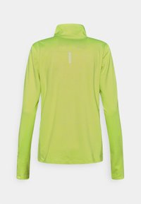 Pitkähihainen paita kirkkaan limetinvihreänä, jossa on korkea kaulus ja heijastavat yksityiskohdat takana. Sileä pinta, slim fit -malli.