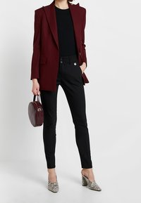 Bordowy żakiet dopasowany do sylwetki na czarnym topie, zestawiony z dopasowanymi czarnymi spodniami. Akcesoria to okrągła bordowa torebka i szpilki w wzór węża.