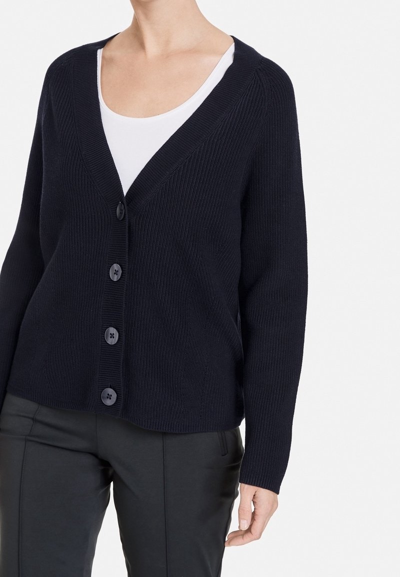 Marineblauer Strickcardigan mit tiefem V-Ausschnitt, langen Ärmeln und sechs dunklen Knöpfen. Er zeichnet sich durch eine gerippte Textur und eine lässige Passform aus.
