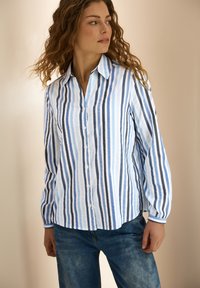 Camicia con bottoni e righe verticali in azzurro chiaro, blu scuro e bianco. Presenta un colletto, maniche lunghe e un tessuto testurizzato.