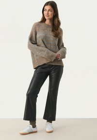 Brauner Strickpullover mit blauen Streifen, weiten Ärmeln und geripptem Saum, kombiniert mit schwarzen, gefälschten Lederhosen und weißen Turnschuhen.