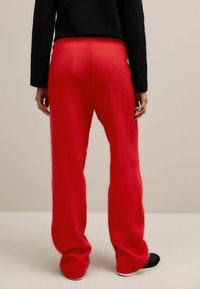 Rode, gebreide, rechte broek met een elastische tailleband. Textuurstof. Gedragen met een zwart langemouwen T-shirt en zwarte schoenen.